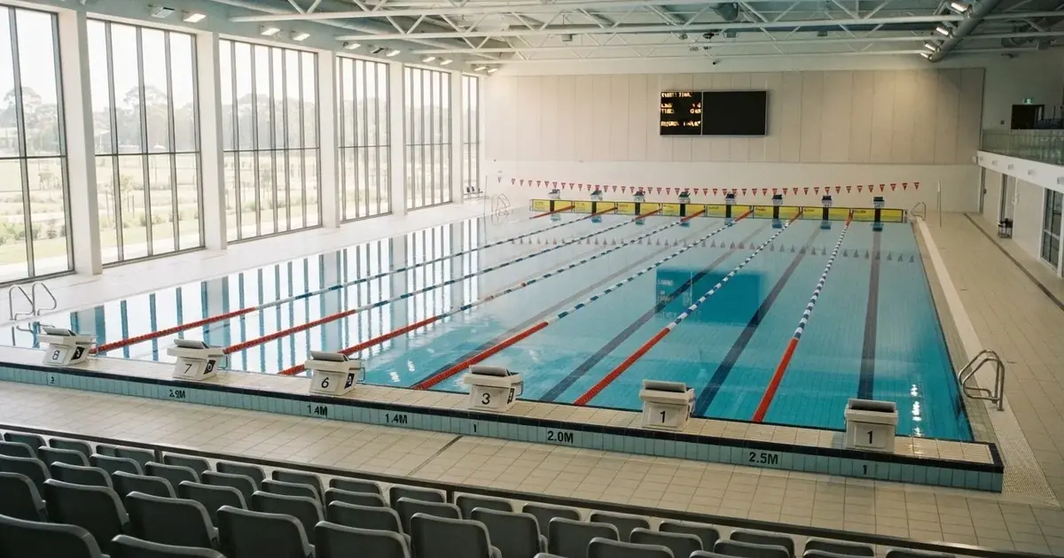 Pusty basen olimpijski z równymi torami i spokojną taflą wody, widok z trybun w jasnym świetle.