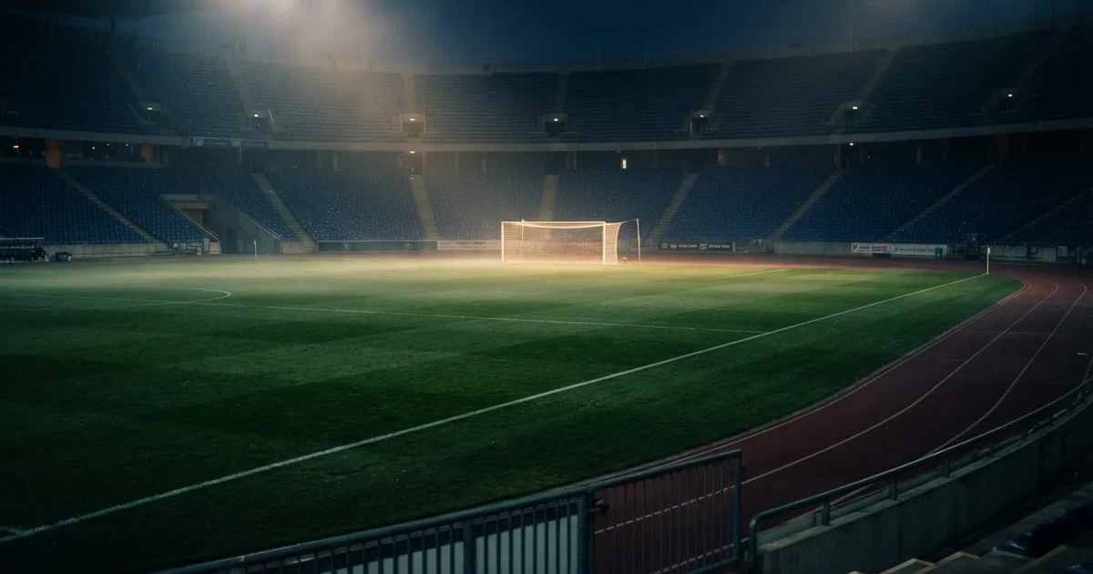 Pusta murawa stadionu miejskiego w chłodny jesienny wieczór, siatka bramki świeci w świetle reflektorów, nad boiskiem wisi mgła.